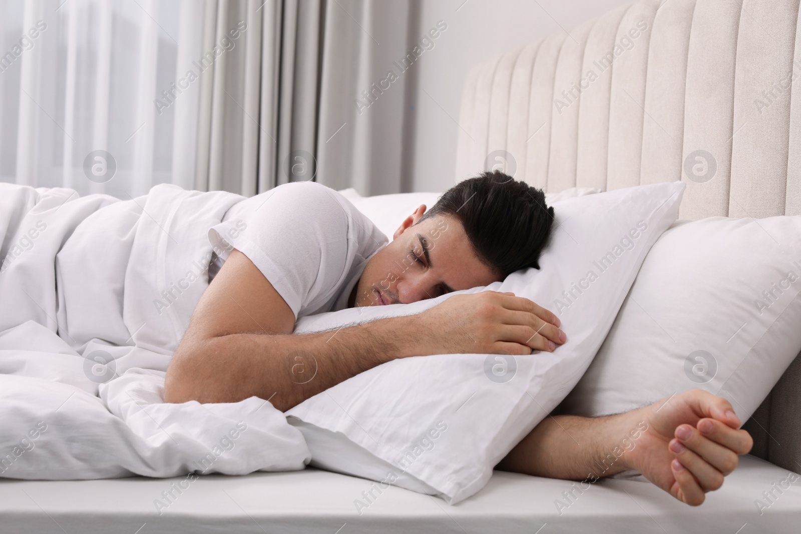 Photo of Handsome man sleeping under pillow in bed at home