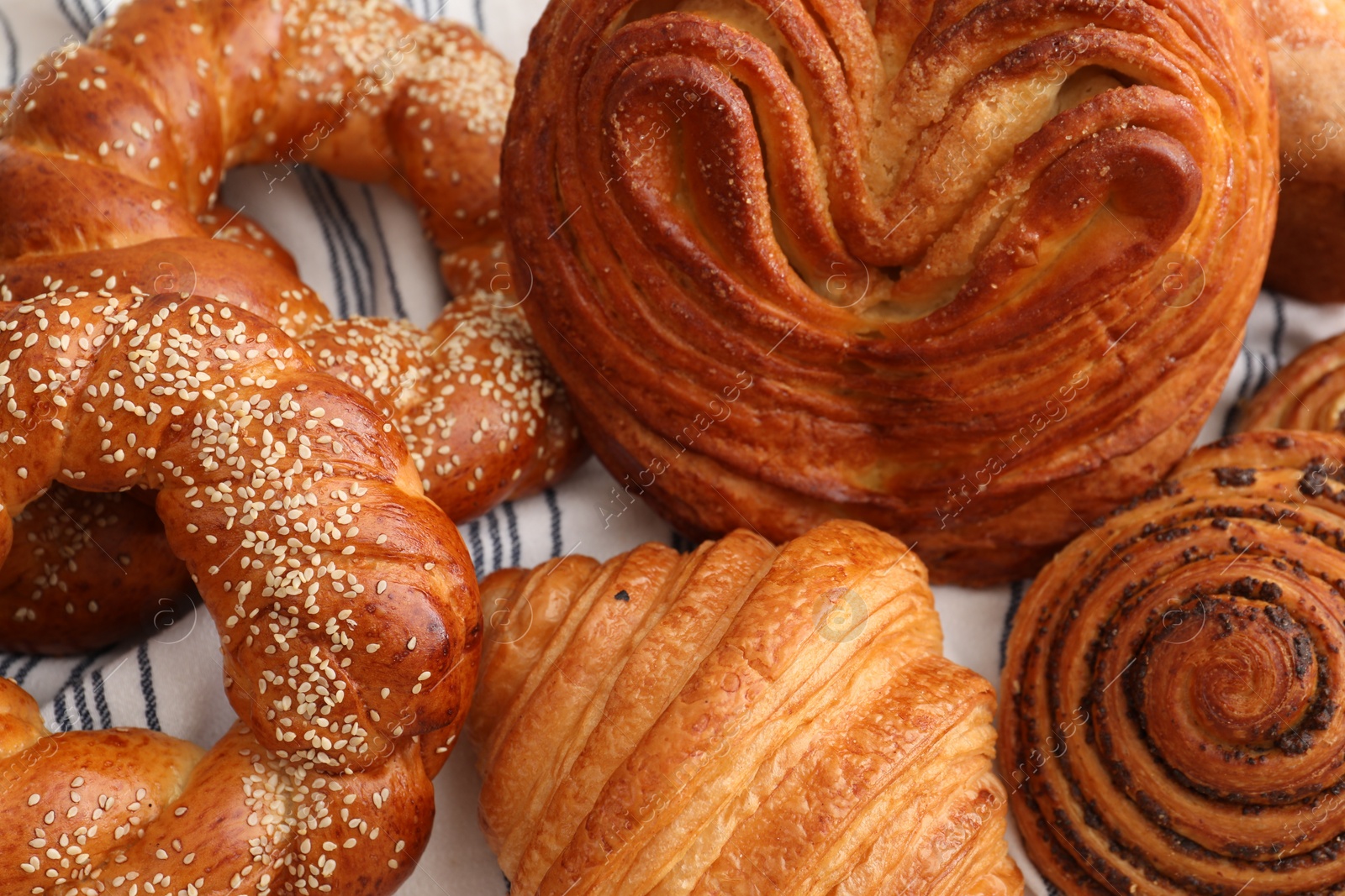 Photo of Different tasty freshly baked pastries on striped tablecloth, closeup