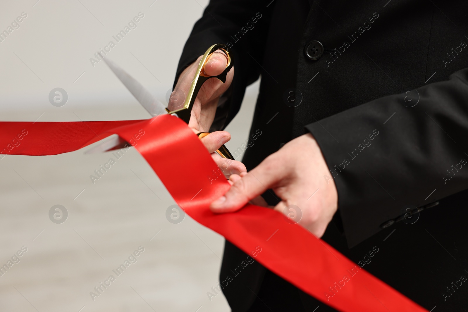 Photo of Man cutting red ribbon with scissors on blurred background, closeup