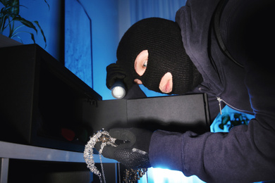 Photo of Thief taking jewelry out of steel safe indoors at night