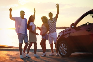 Happy friends near car outdoors at sunset. Summer trip