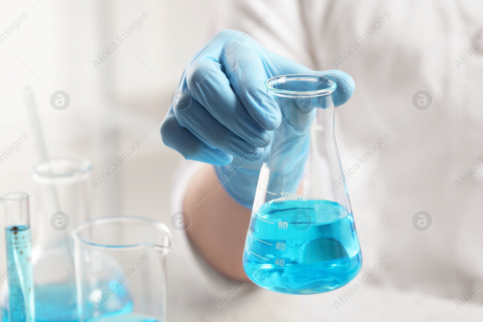 Photo of Scientist with flask of light blue liquid in laboratory, closeup