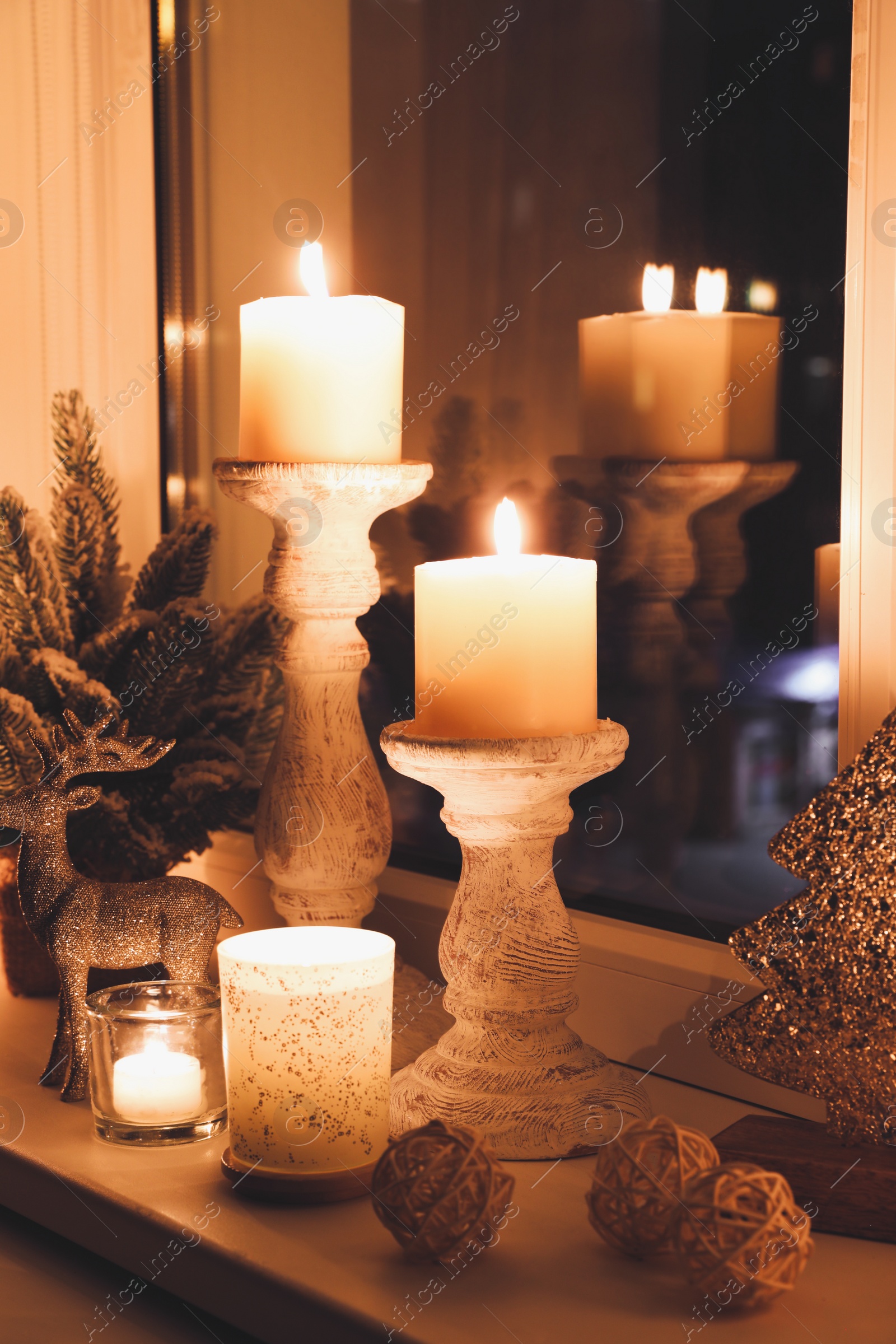 Photo of Burning candles and Christmas decor on window sill at night