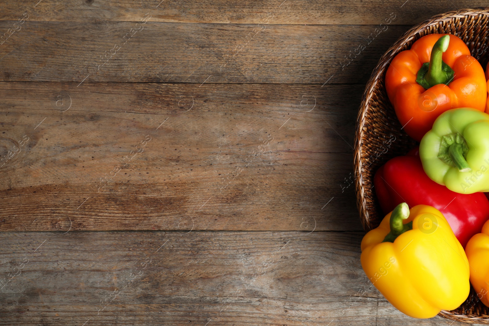 Photo of Wicker bowl with ripe bell peppers on wooden table, top view. Space for text