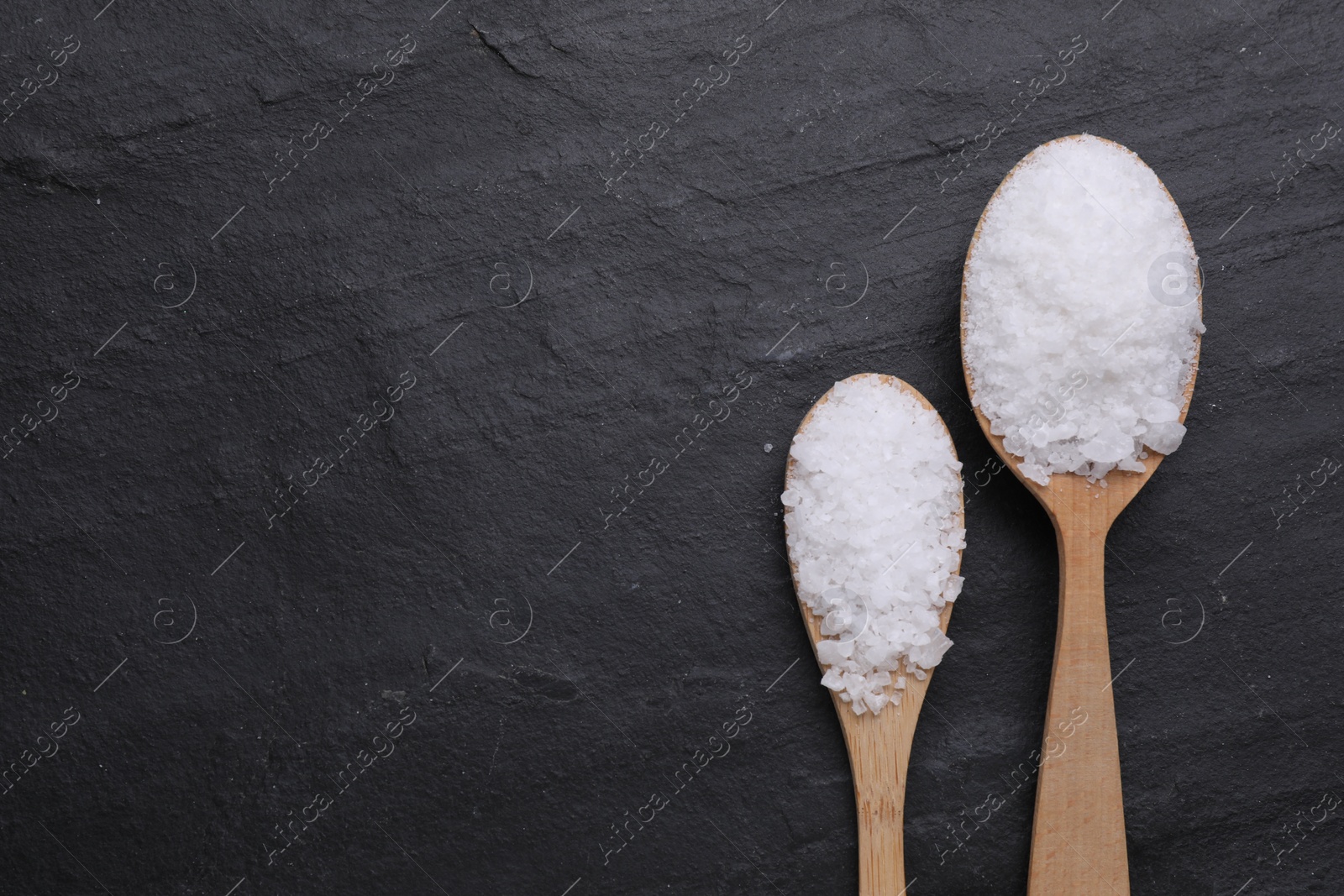 Photo of Spoons with sea salt on black table, flat lay. Space for text