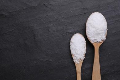 Photo of Spoons with sea salt on black table, flat lay. Space for text