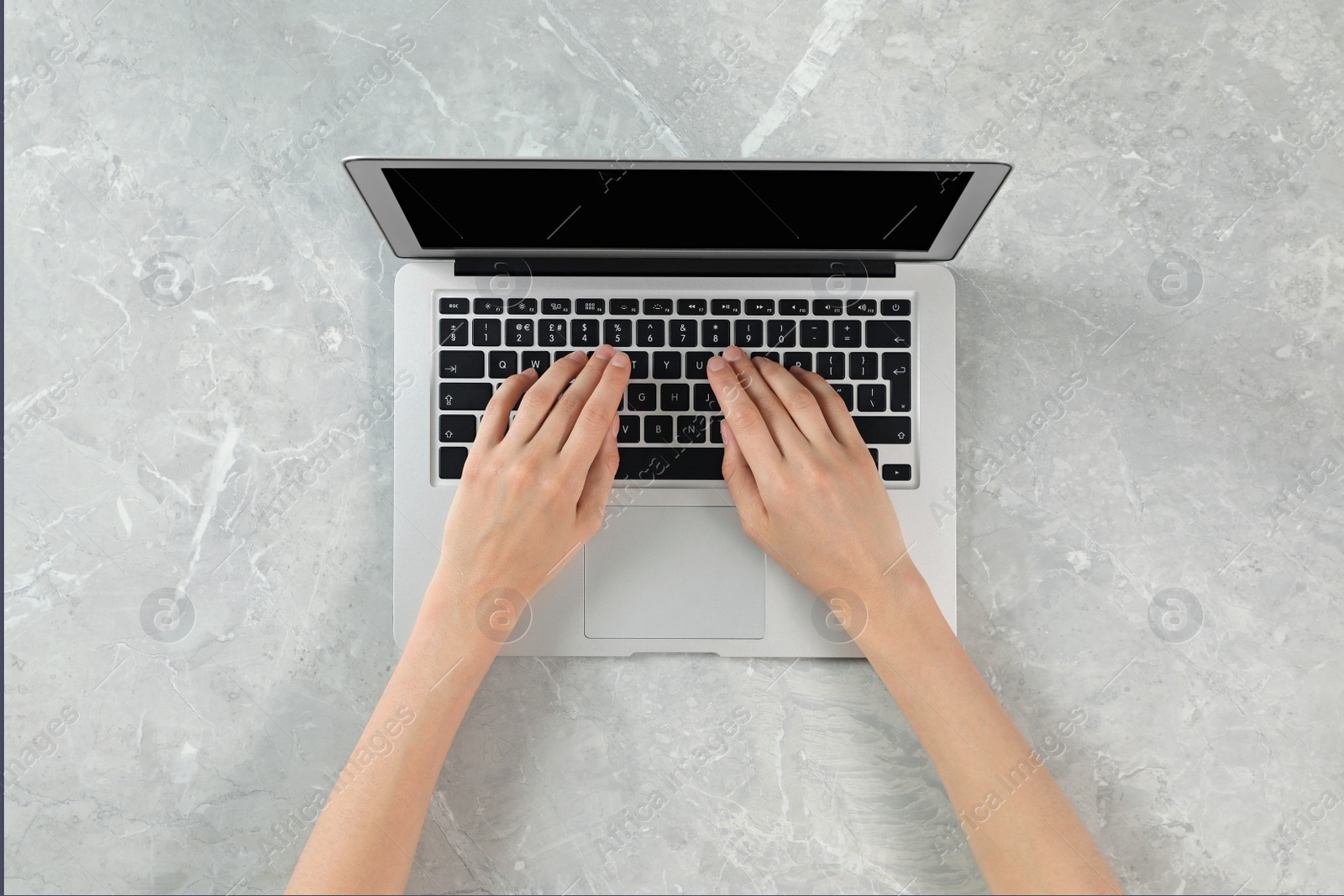 Photo of Woman using modern laptop at marble table, top view