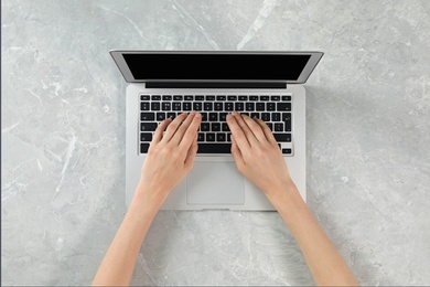 Woman using modern laptop at marble table, top view