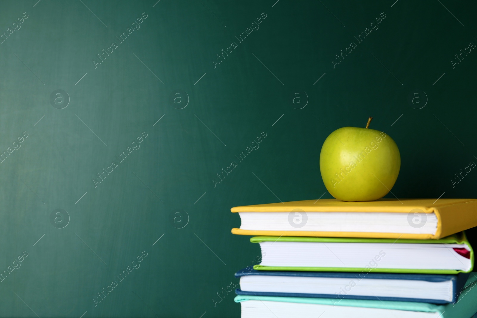 Photo of Books and apple near green chalkboard, space for text. School education