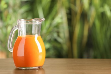 Jug with tasty carrot juice on wooden table outdoors. Space for text