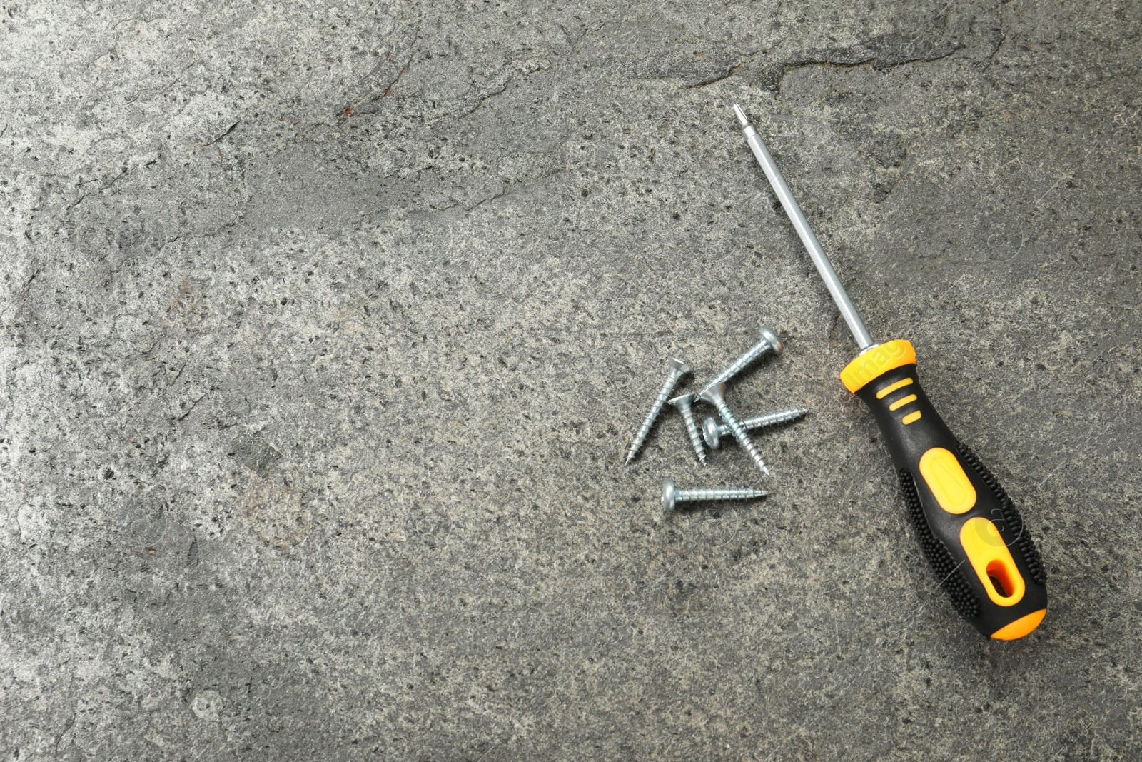 Photo of Screwdriver with black handle and screws on grey textured table, flat lay. Space for text