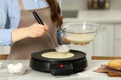 Woman cooking delicious crepe on electric maker at white marble table in kitchen, closeup