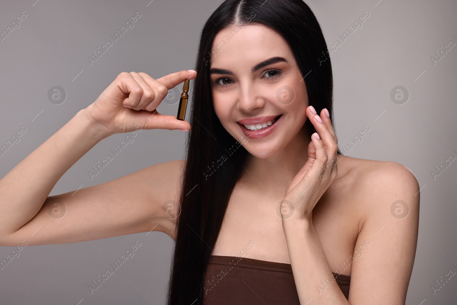 Photo of Beautiful young woman holding skincare ampoule on grey background