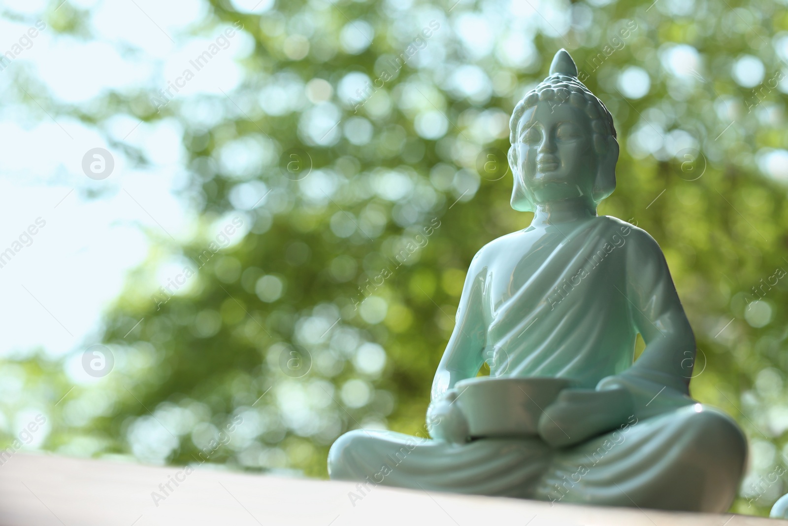 Photo of Beautiful ceramic Buddha sculpture on blurred background, closeup. Space for text