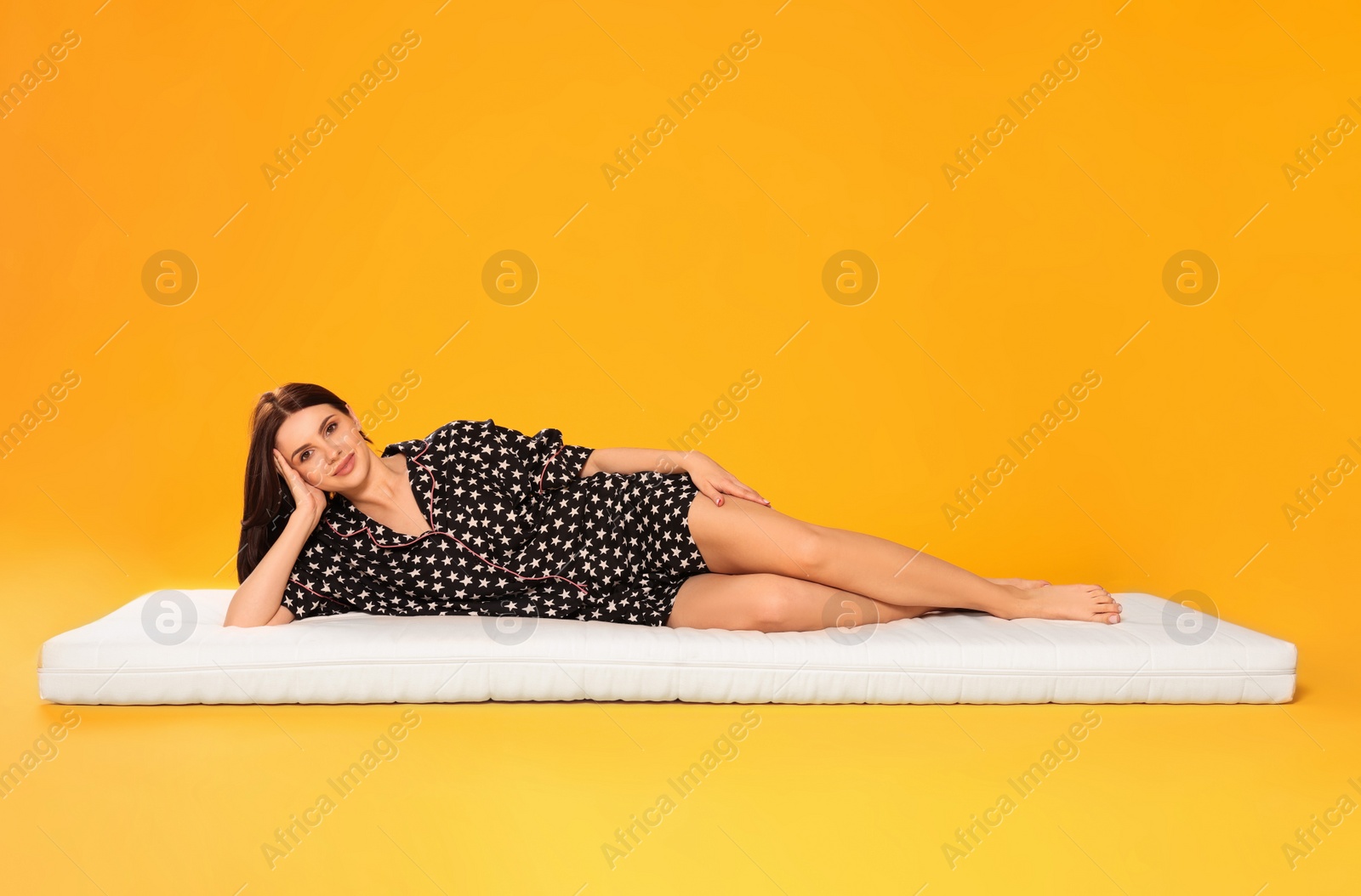 Photo of Young woman lying on soft mattress against orange background