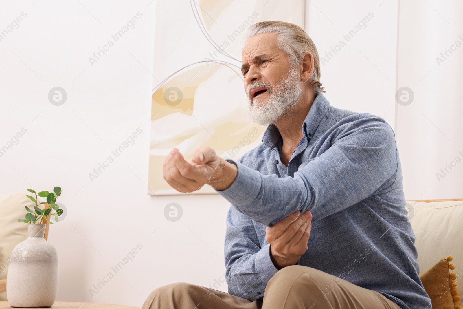 Photo of Senior man suffering from pain in his elbow at home. Arthritis symptoms