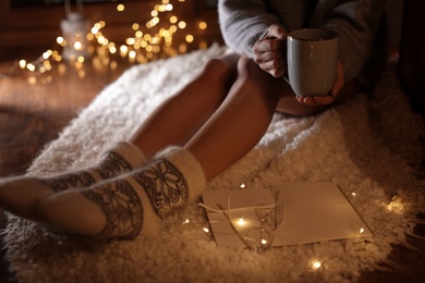 Woman with cup of hot beverage and book at home in winter evening, closeup