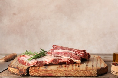Photo of Wooden board with raw meat and rosemary on table against grey background. Space for text