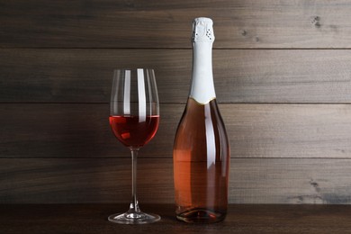 Bottle and glass of delicious rose wine on table against wooden background