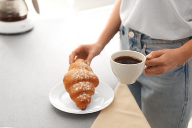 Photo of Woman having tasty breakfast with croissant and coffee at home, closeup. Morning routine