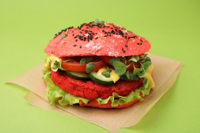 Photo of Tasty pink vegan burger with vegetables, patty and microgreens on light green background, closeup