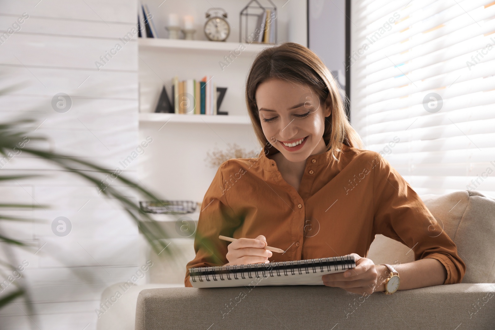 Photo of Young woman drawing in sketchbook with pencil at home, space for text