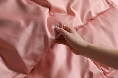 Photo of Woman making bed with beautiful pink silk linens, closeup view