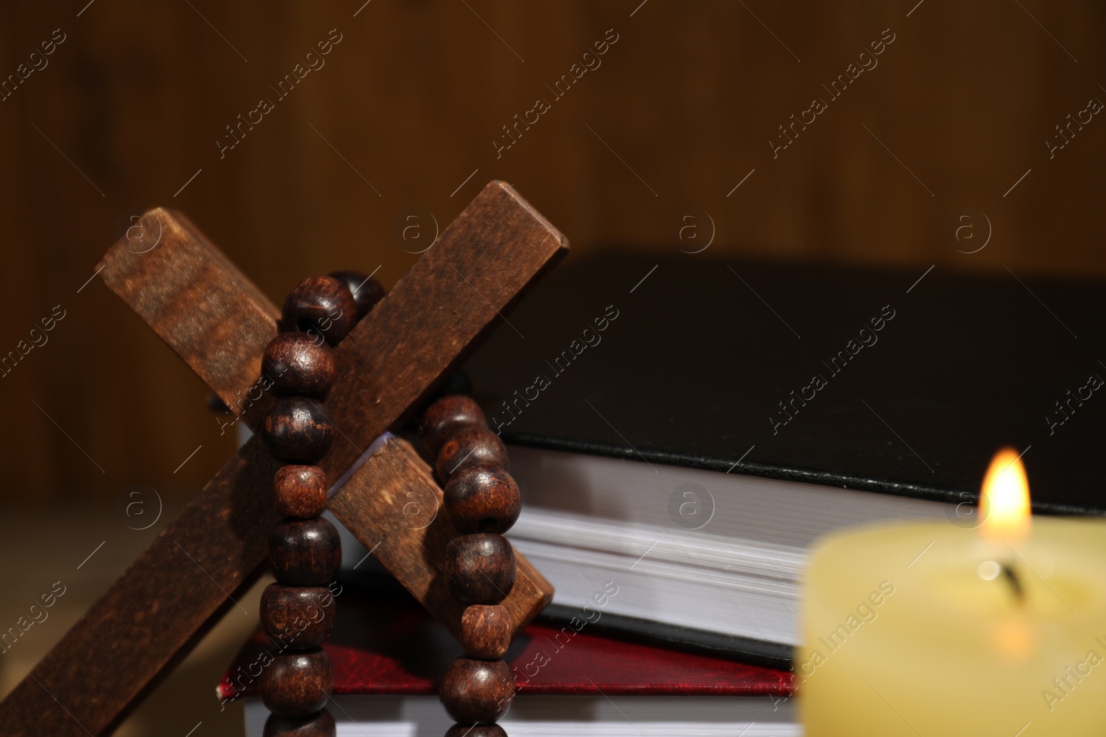 Photo of Bible, wooden cross, rosary beads and church candle on table, closeup