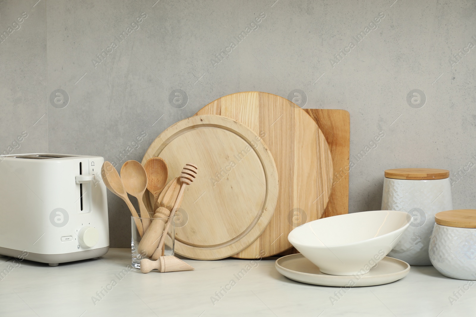 Photo of Different wooden cutting boards, toaster and other cooking utensils on white countertop in kitchen