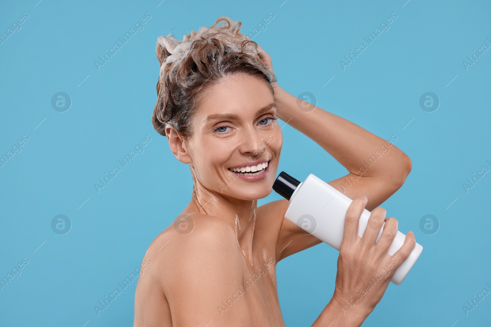 Photo of Portrait of beautiful happy woman with bottle singing while washing hair on light blue background