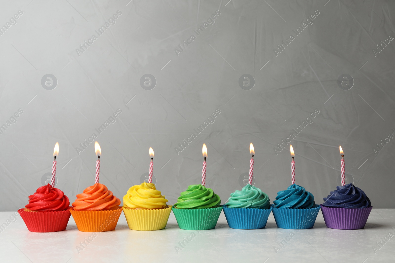 Photo of Delicious birthday cupcakes with burning candles on table