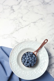 Photo of Dishware with juicy and fresh blueberries on marble table, top view. Space for text