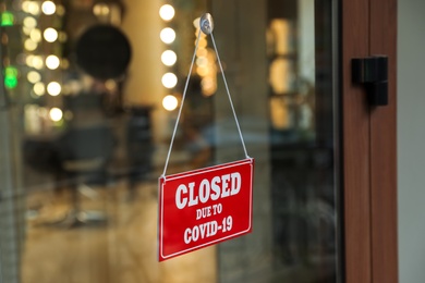 Photo of Red sign with words Closed Due To Covid-19 hanging on glass door