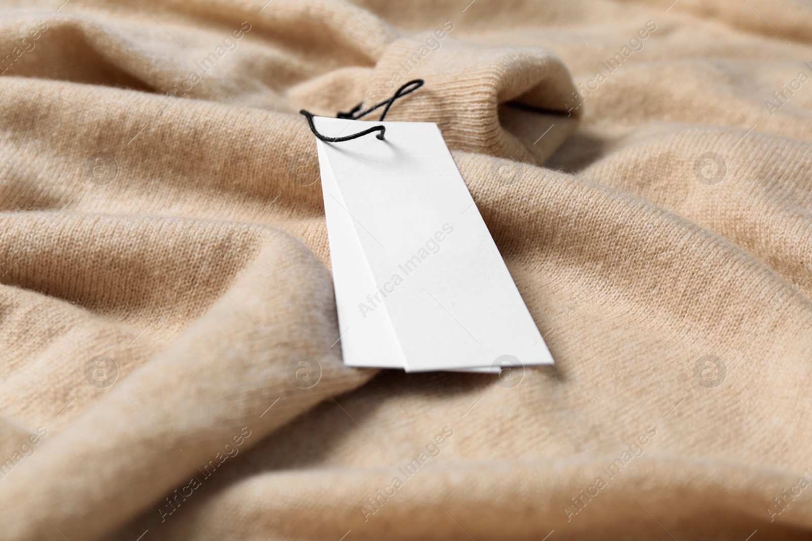 Photo of Blank white tags on beige sweater, closeup. Space for text