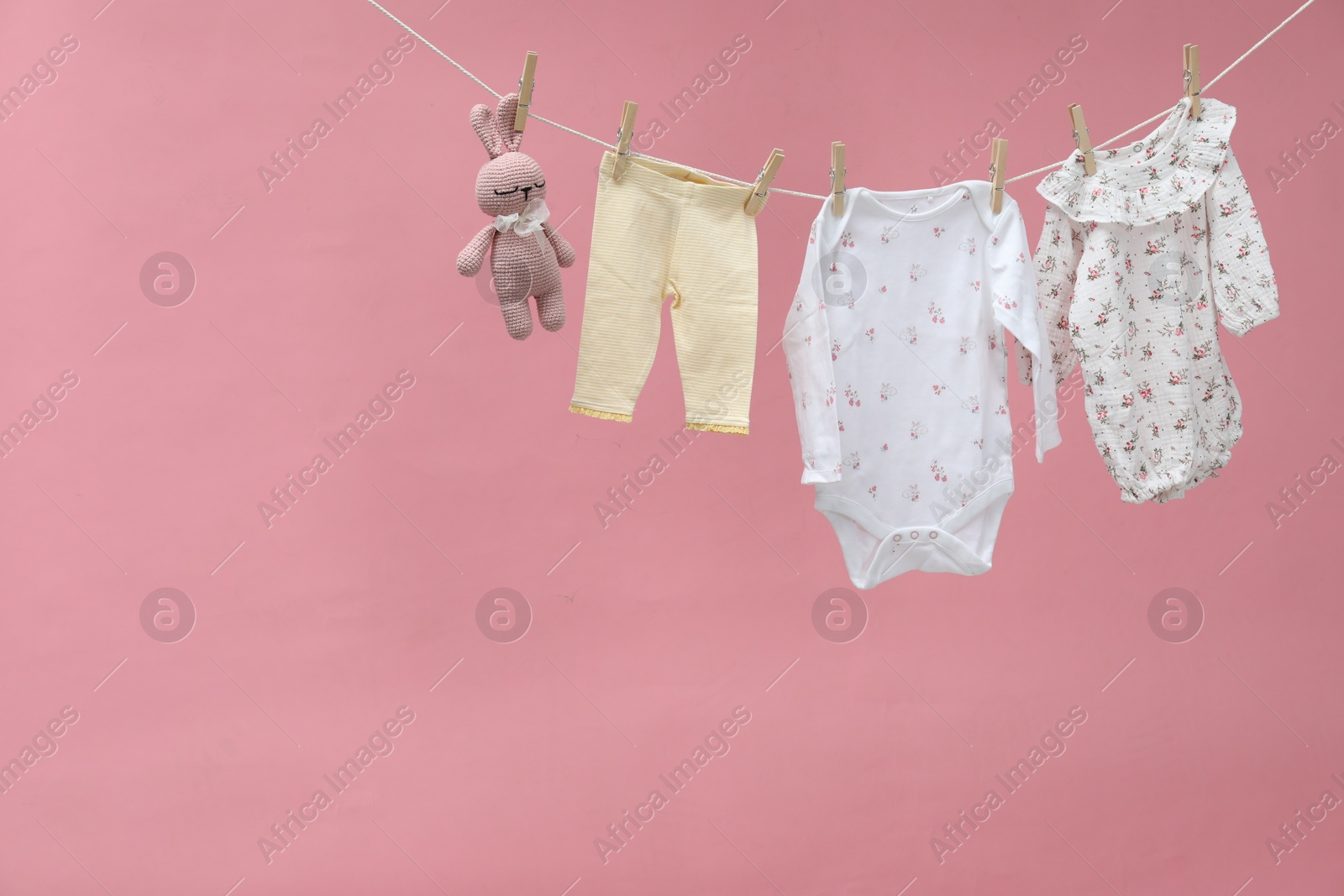 Photo of Different baby clothes and bunny toy drying on laundry line against pink background. Space for text