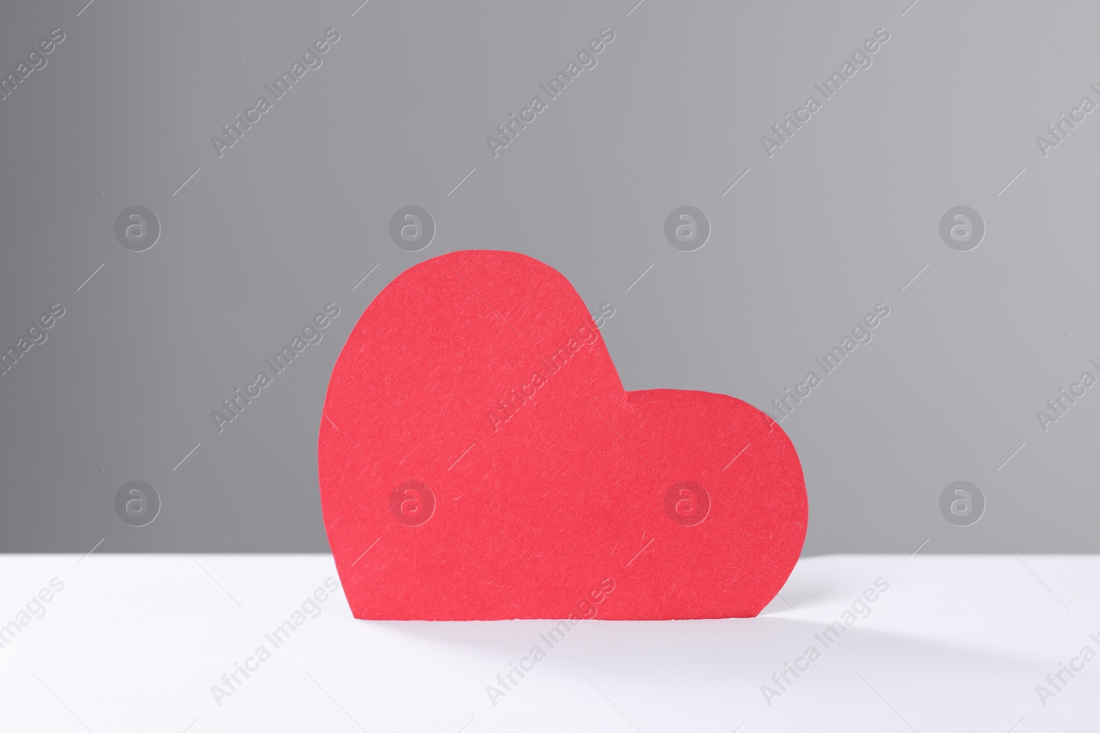 Photo of Red heart into slot of donation box against grey background