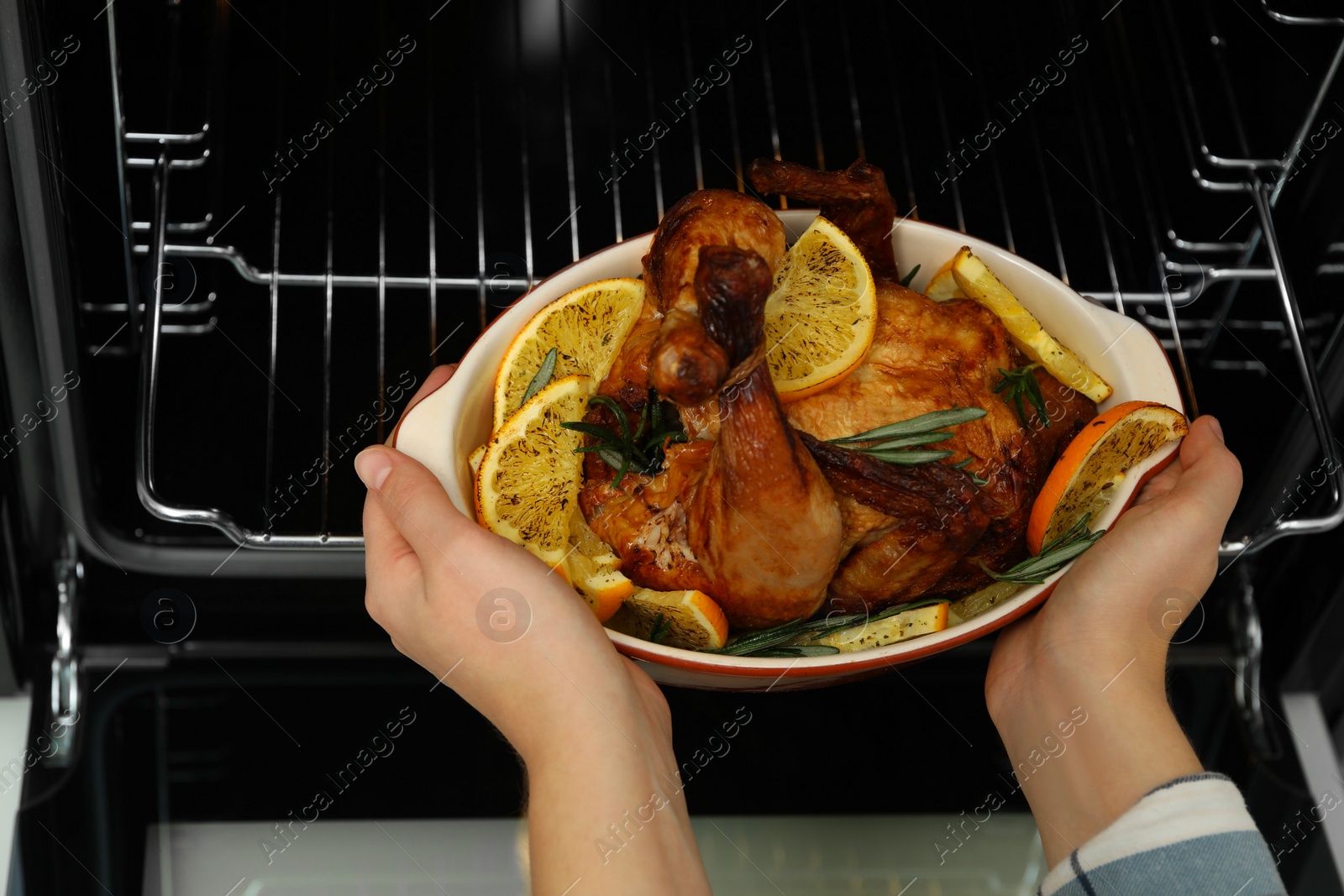 Photo of Woman taking baked chicken with orange slices out of oven, closeup