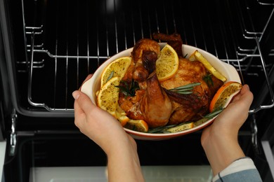 Photo of Woman taking baked chicken with orange slices out of oven, closeup