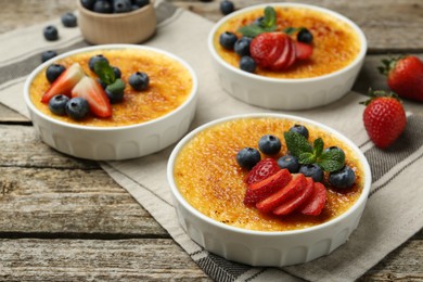 Photo of Delicious creme brulee with berries and mint in bowls on wooden table, closeup