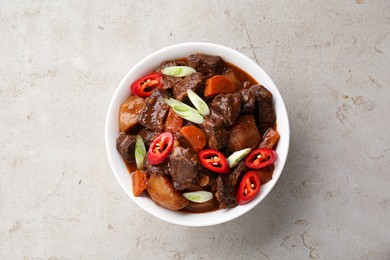 Photo of Delicious beef stew with carrots, chili peppers, green onions and potatoes on white textured table, top view