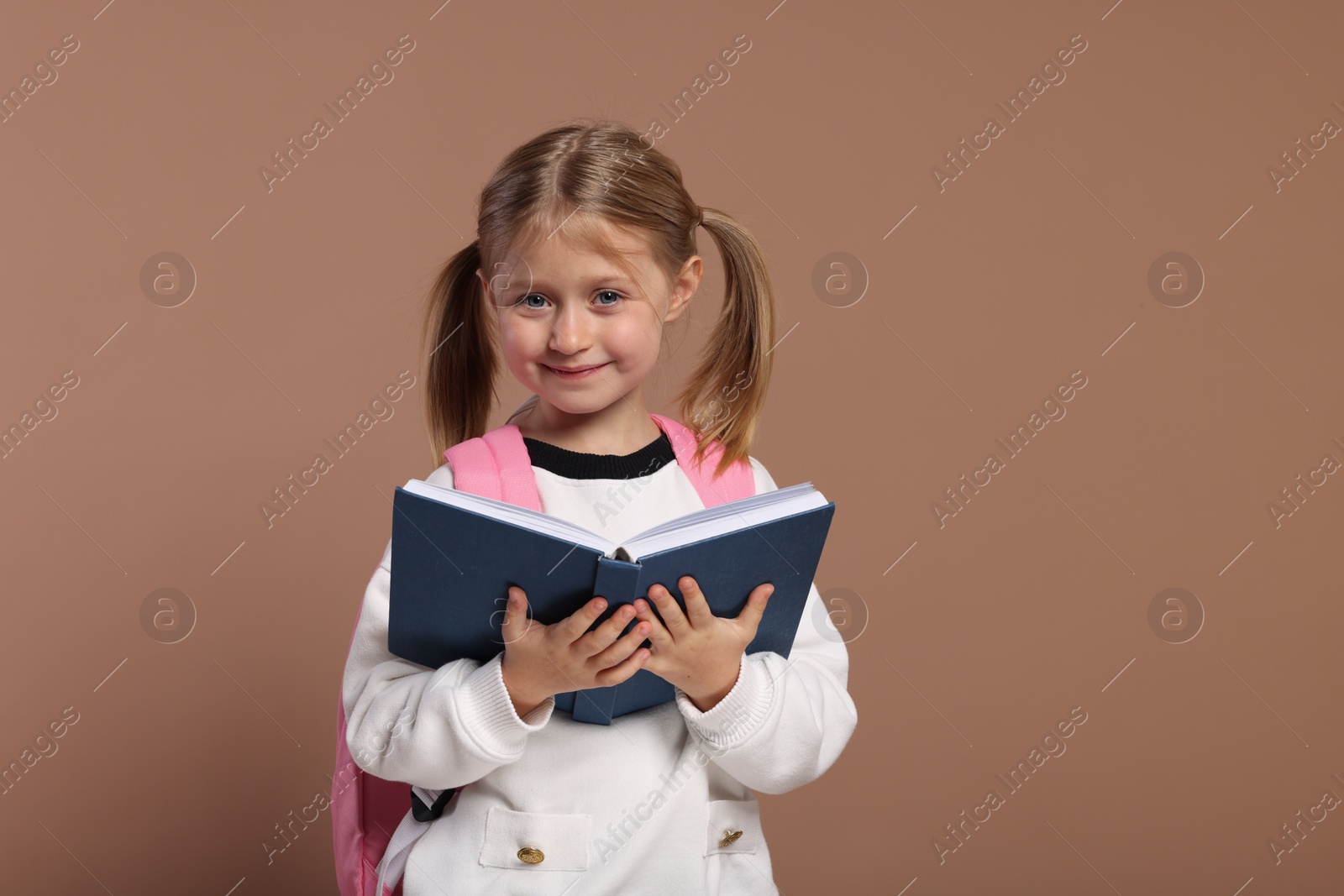 Photo of Happy schoolgirl with backpack and book on brown background