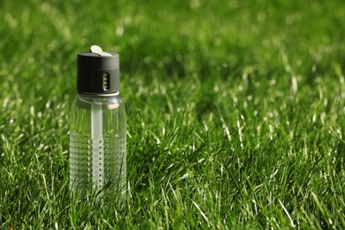 Sport bottle of water on green grass, space for text