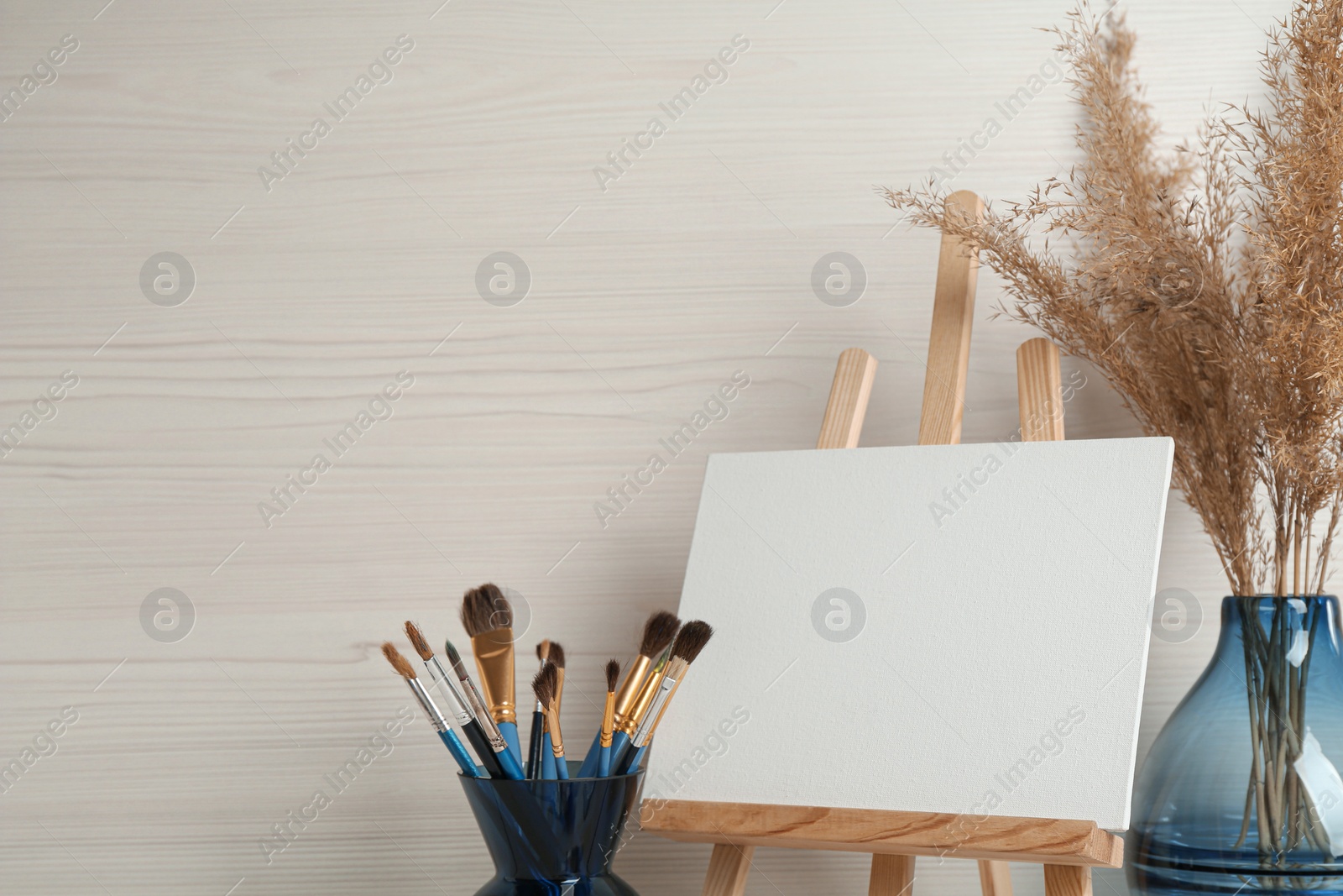 Photo of Easel with blank canvas and brushes in studio. Space for text