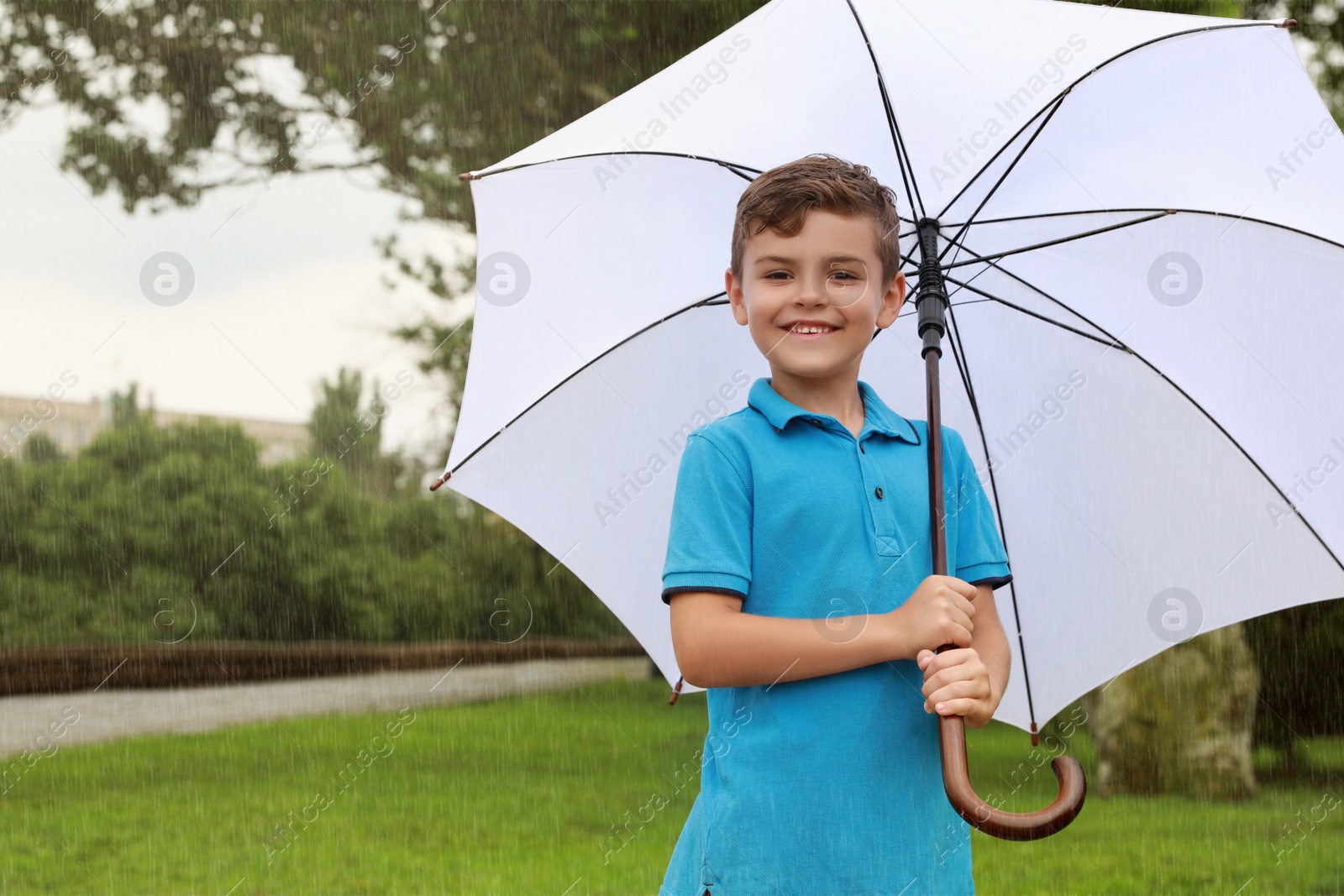 Photo of Little boy with umbrella walking under rain in park