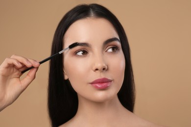 Photo of Woman applying makeup with eyebrow brush on light brown background