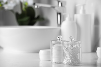 Photo of Containers with cotton swabs and pads on white countertop in bathroom. Space for text