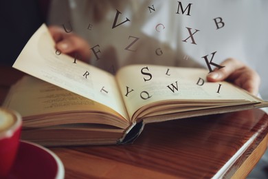Image of Woman reading book with letters flying over it at table indoors, closeup