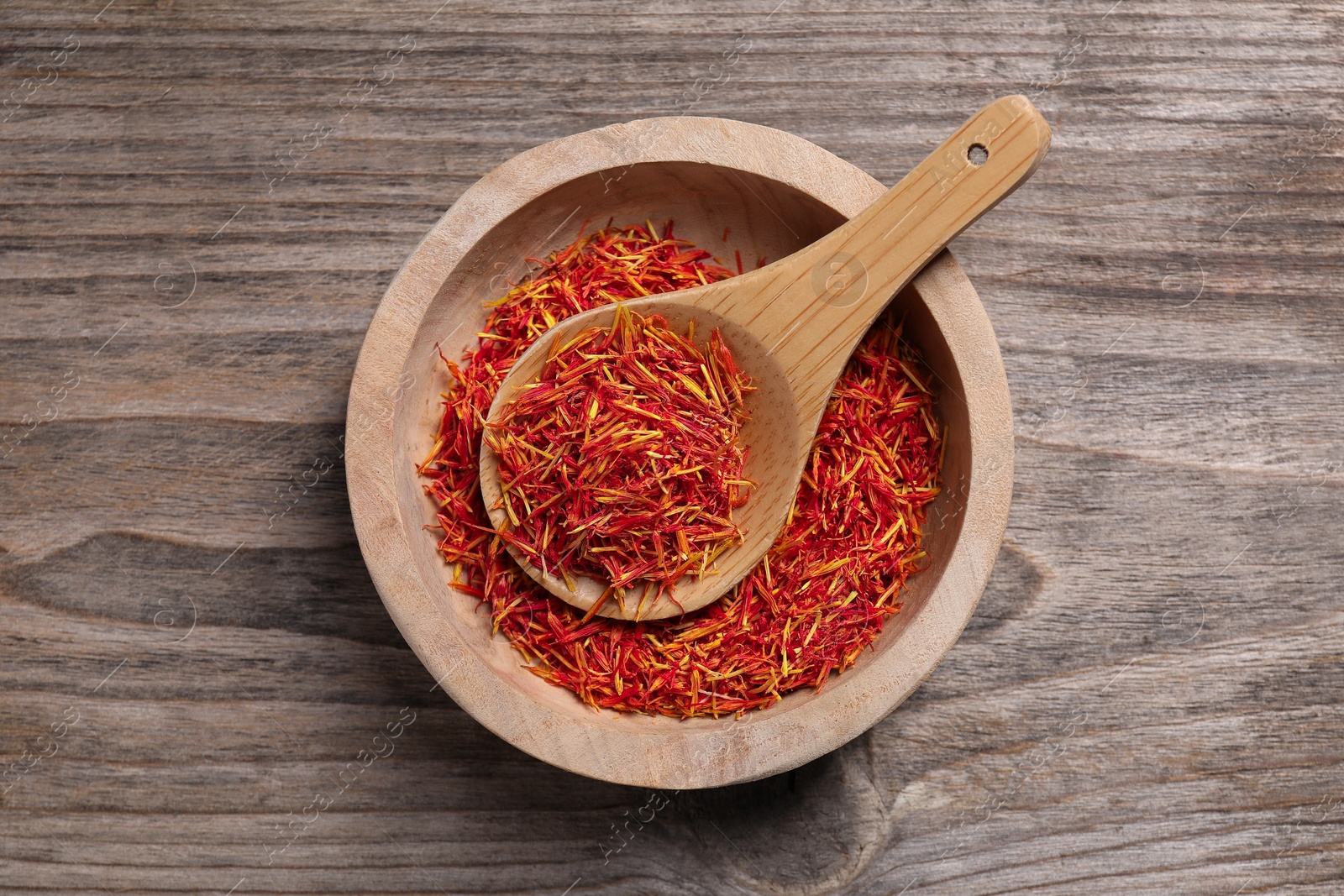 Photo of Aromatic saffron in bowl and spoon on wooden table, top view