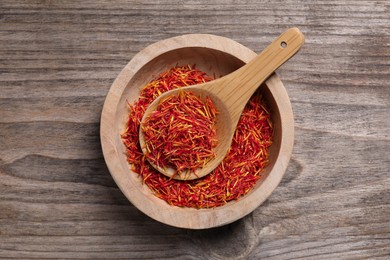 Aromatic saffron in bowl and spoon on wooden table, top view