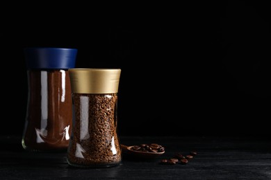 Glass jars with aromatic instant and ground coffee near beans on black wooden table. Space for text